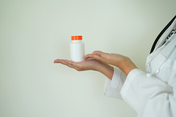 An asian young doctor with stethoscope is holding an medicine bottle to assess the quality of medicine, recommending medication  to patient and explaining the dose and description of the medication.