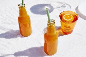 Cold summer drink. Refreshing fresh orange juice in bottles with drinking straw on the table with white tablecloth.