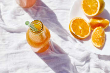 Cold summer drink. Refreshing fresh orange juice in bottles with drinking straw on the table with white tablecloth.