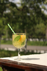 Lemonade on a blurred nature background. Close-up of a glass with a cocktail outdoors. Lemonade or other drink in a glass. Summer refreshing drink with mint and orange slices
