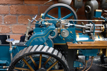 Vintage mechanical steam engine with visible gears and levers against a brick wall.
