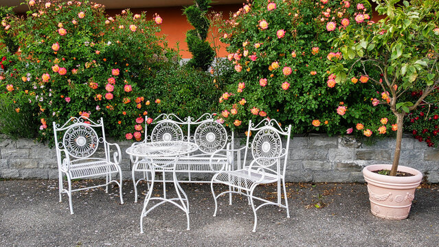 Gem&uuml;tliche Sitzecke auf einer Gartenterrasse und umgeben von bl&uuml;henden Rosen