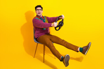 Young man in stylish casual attire holding a steering wheel and posing playfully against a vibrant yellow background