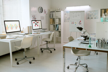 Contemporary laboratory with white walls and furnishing featuring desktop computers, scientific diagrams, and laboratory equipment for conducting research and analysis