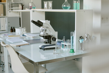 Laboratory desk displaying microscope and various research equipment, surrounded by beakers, test tubes, and notebooks, indicating space for scientific work and experiments