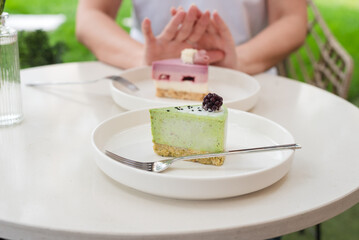 Woman Gesturing Near Colorful Cakes on White Plates in Outdoor Setting. No to sugar, diet concept, fasting, dieting, losing weight. No cakes, woman on a diet.