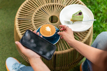 Close-up of a woman holding a cappuccino with latte art and a smartphone during a relaxing outdoors...