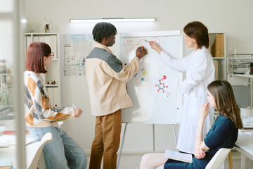 Group of multiracial classmates collaborating on project, drawing on whiteboard and discussing...