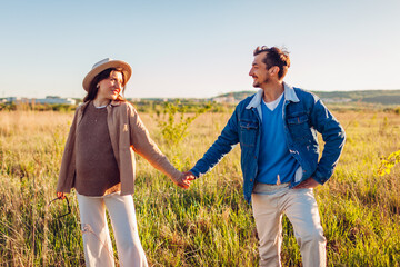 Stylish pregnant family couple walking outdoors. Future parents in love hugging enjoying sunset. Man and woman holding hands