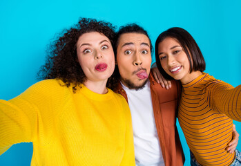 Three young friends making funny faces in front of a blue background capturing a fun moment of...