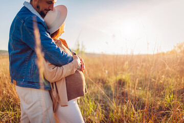 Portrait of pregnant family couple walking outdoors. Future parents in love hugging enjoying sunset. Woman showing her baby bump