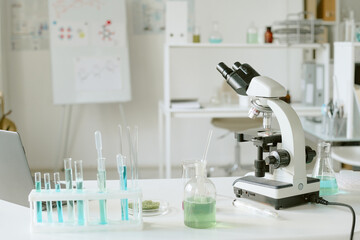 Scientific laboratory featuring microscope and various test tubes with colored liquids. Focus on scientific research equipment in bright, clean workspace