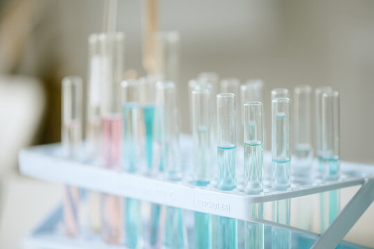 Close up of multiple test tubes containing various colored liquids placed in laboratory rack, with a blurred background. Creating scientific and experimental setting
