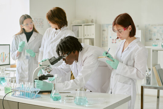 Team of scientists working in modern laboratory, examining samples, and recording data. Diverse group wearing lab coats and safety goggles, surrounded by various scientific instruments