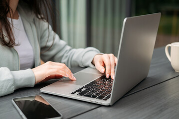 Close-up of hands typing on a laptop outdoors with a coffee mug and tablet on the table.