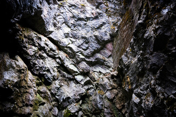 The rough, uneven walls of the cave made of marble-limestone close into a corner. It is illuminated from above by natural diffused light through an artificial crevice.