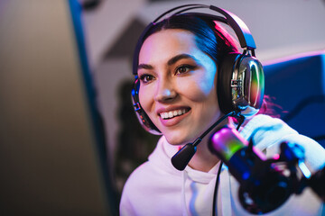 Young woman enjoying online gaming with vibrant neon lighting while streaming from home during an...