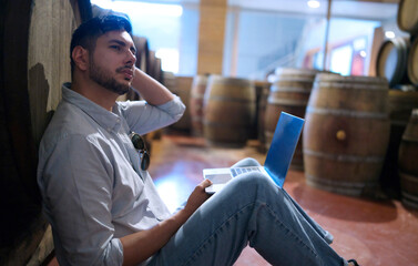 Professional man winemaker working and inspecting wine quality in cellar with wooden barrel in factory. Winery manufacturing industry, Alcohol and winemaking fermentation process.