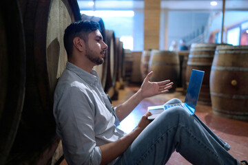 Professional man winemaker working and inspecting wine quality in cellar with wooden barrel in factory. Winery manufacturing industry, Alcohol and winemaking fermentation process.