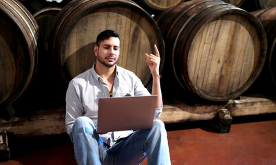 Professional man winemaker working and inspecting wine quality in cellar with wooden barrel in factory. Winery manufacturing industry, Alcohol and winemaking fermentation process.