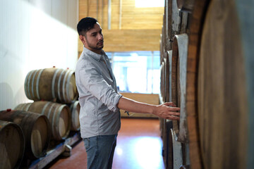 Professional man winemaker working and inspecting wine quality in cellar with wooden barrel in factory. Winery manufacturing industry, Alcohol and winemaking fermentation process.