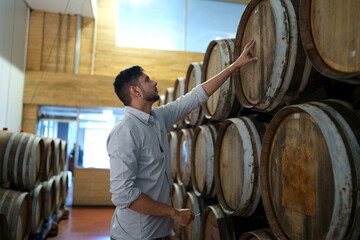 Professional man winemaker working and inspecting wine quality in cellar with wooden barrel in factory. Winery manufacturing industry, Alcohol and winemaking fermentation process.