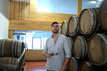 Professional man winemaker working and inspecting wine quality in cellar with wooden barrel in factory. Winery manufacturing industry, Alcohol and winemaking fermentation process.