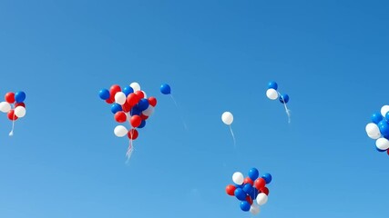 Colorful balloons in red, white, and blue ascending into a clear blue sky during a festive event