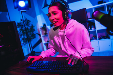 Female gamer passionately playing video games in a colorful neon-lit room during an immersive gaming session.