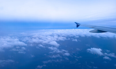Plane flying over clouds, aerial view from airplane window, fluffy cloudscape and blue sky