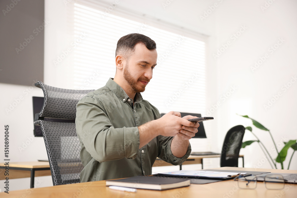 Poster man taking photo of document using scanning app on smartphone at desk in office