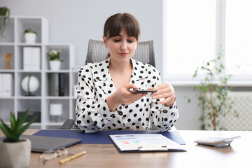 Woman taking photo of document using scanning app on smartphone at desk in office