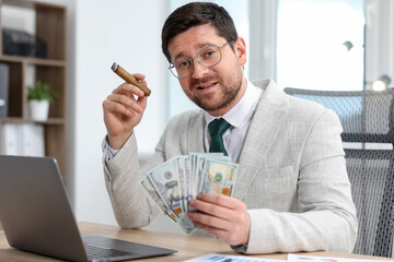 Greedy banker with dollar banknotes and cigar at table in office