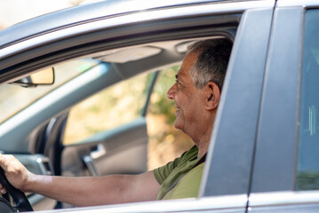 A middle-aged man enjoys a relaxed moment behind the wheel with the car window open. Captured from a side angle, the image evokes authentic travel, freedom, and everyday driving experience.