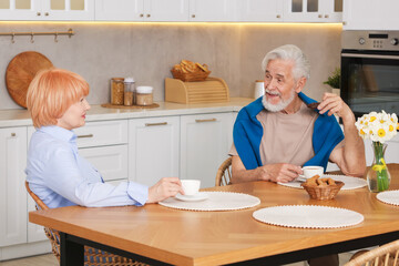 Obraz premium Lovely senior couple having breakfast together at wooden table in kitchen