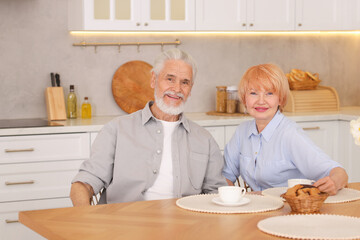 Lovely senior couple having breakfast together at wooden table in kitchen