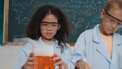Closeup of Energetic cute girl inspect solution while looking at sample. Curious american student standing at blackboard with chemical theory while doing experiment and discovery new sample. Pedagogy.