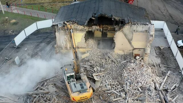 Aerial drone timelapse video of  Yellow excavator destroys building. Heavy duty machine is demolishing a brick building. Demolition of the building . Demolition construction work.