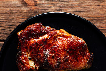 Juicy grilled steak resting on a black plate against a rustic wooden background