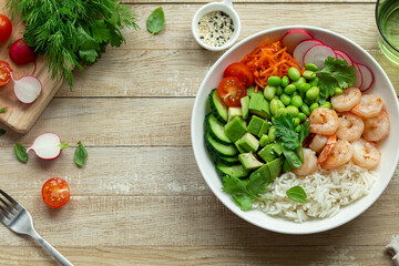 lunch bowl with rice, shrimps, avocado, cucumber, edamame beans radish and tomato in white bowl