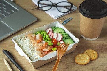 lunch break.Rice with shrimps and vegetables in paper take away box on desk