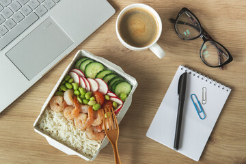 Lunch time. Rice with shrimps and vegetables in paper take away box on desk