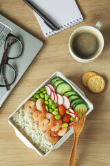 Lunch time. Rice with shrimps and vegetables in paper take away box on desk