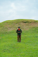 A male adventurer is enjoying the beauty of a small hill covered in green grass. The Asian male traveler is relaxing on the clean and beautiful green hills.