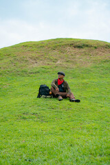 The Asian male traveler sits and relaxes with the charm of clean and beautiful green hills. Concept photo of male tourists doing various poses while enjoying the beauty of green hills.
