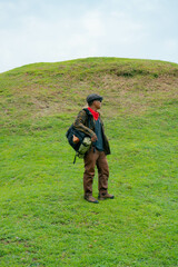 A male adventurer is enjoying the beauty of a small hill covered in green grass. The Asian male traveler is relaxing on the clean and beautiful green hills.