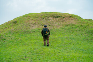 A male adventurer is enjoying the beauty of a small hill covered in green grass. The Asian male traveler is relaxing on the clean and beautiful green hills.