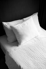 Bed in a hotel room with white sheets, two pillows, and neatly arranged.