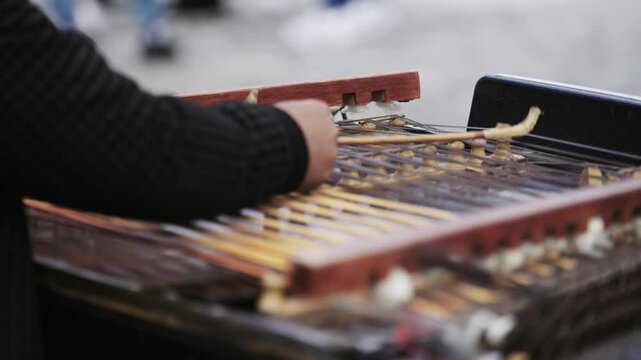 Street performer play traditional cymbal musical instrument with sticks over strings, slow motion