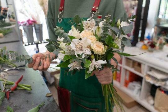 Forist arranging a delicate bouquet of white and peach flowers with eucalyptus branches in a floral studio